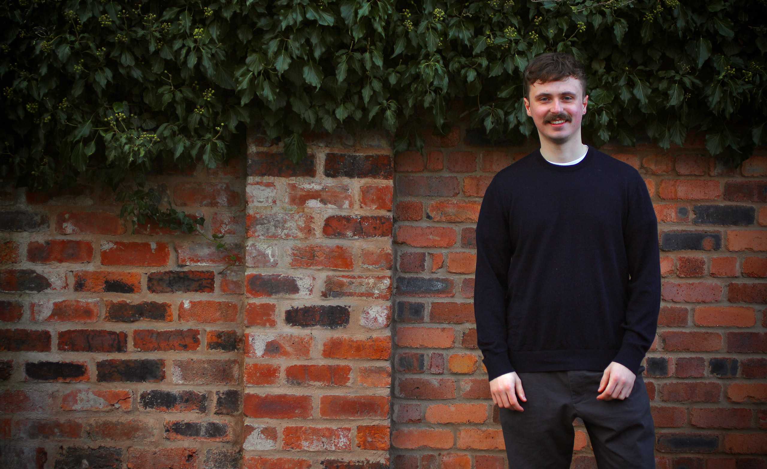 Toby Lyons wearing a sweater stood in front of a brick wall